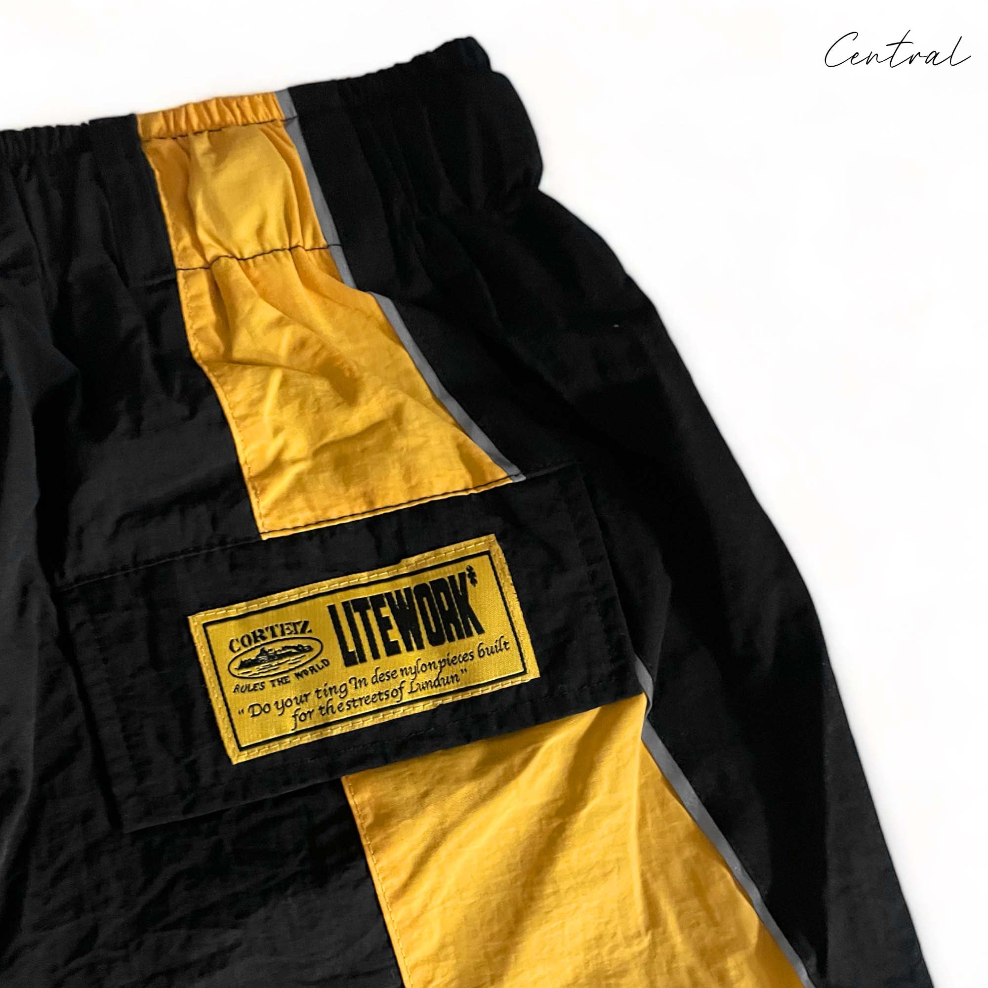 Black and yellow Corteiz shorts from Central ae displayed on a flat surface, showcasing the stylish design and fabric texture.