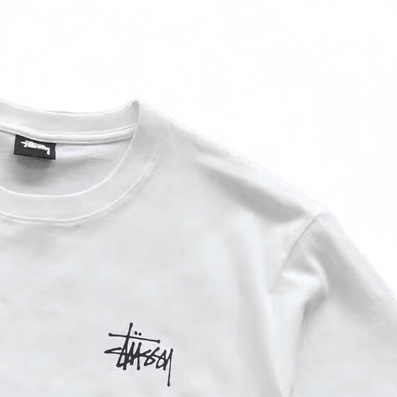 White BASIC STÜSSY TEE featuring a relaxed fit and logo detail, displayed on a plain background.