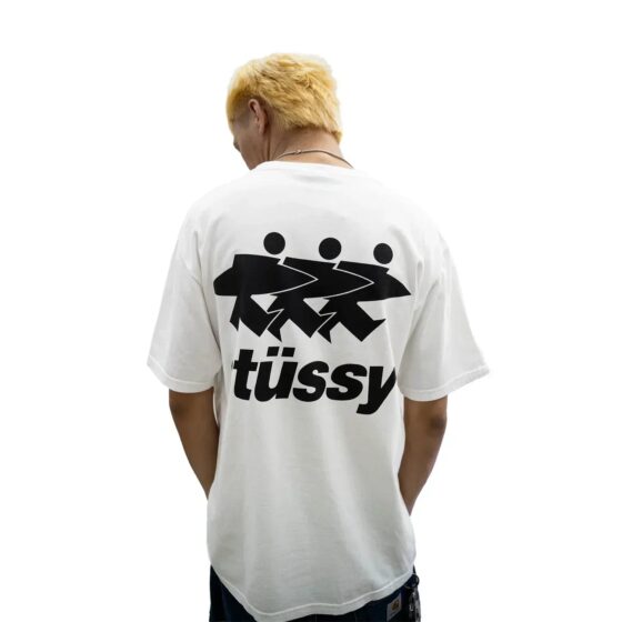 Model wearing a Stussy SURFWALK t-shirt in natural color, showcasing the back design in a casual setting.